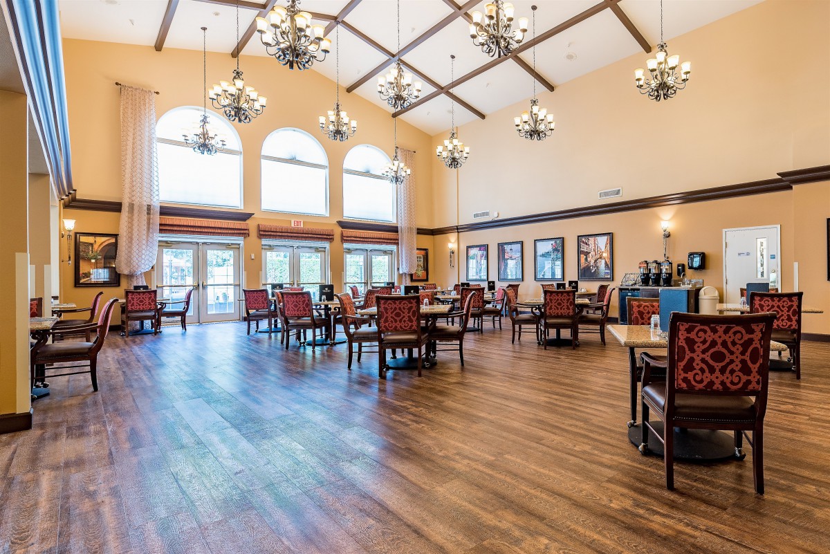 A spacious dining area with chandeliers, wooden flooring, and natural light from large windows.