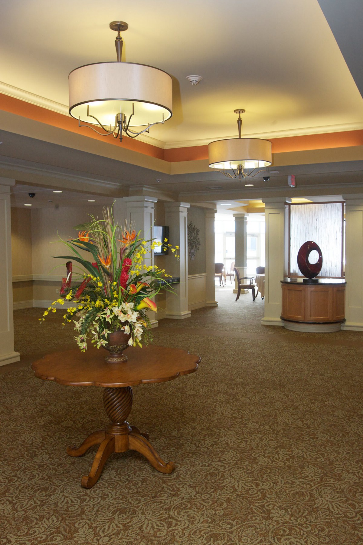 A well-decorated lobby featuring a central table with a floral arrangement, elegant lighting fixtures, and inviting interior decor.