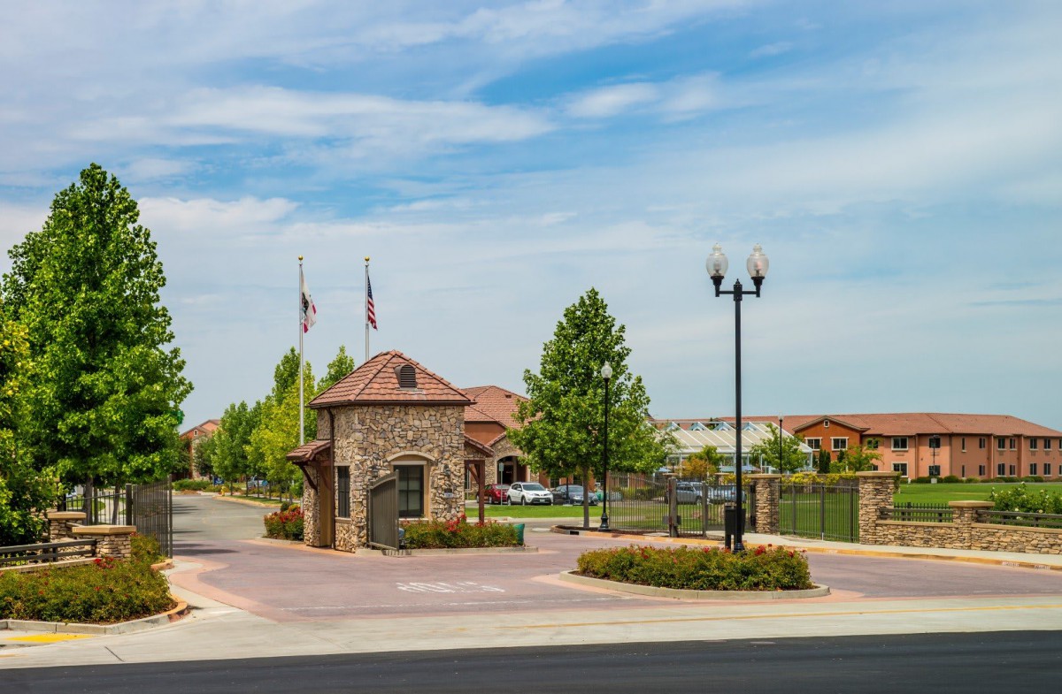 Entrance to a gated suburban community with a stone building and flags.