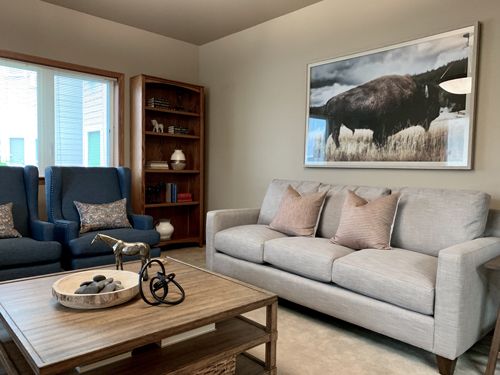 A cozy living room featuring a comfortable sofa, an armchair, and a stylish coffee table with decorative items. A large artwork hangs on the wall above the couch.