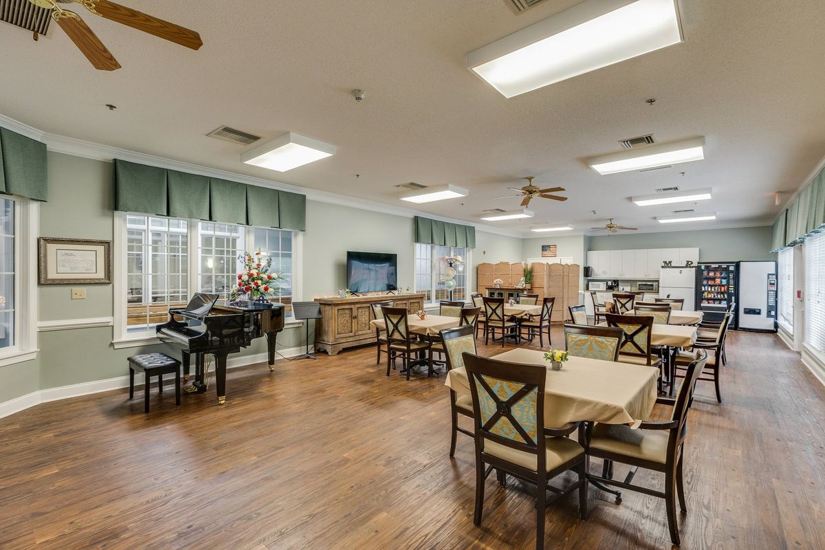 A spacious community dining area with tables, chairs, a piano, and a television.