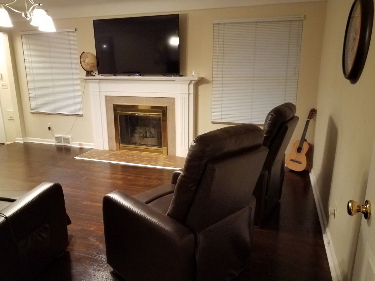 A cozy living room with a fireplace, TV, armchairs, and a guitar against a wooden floor.