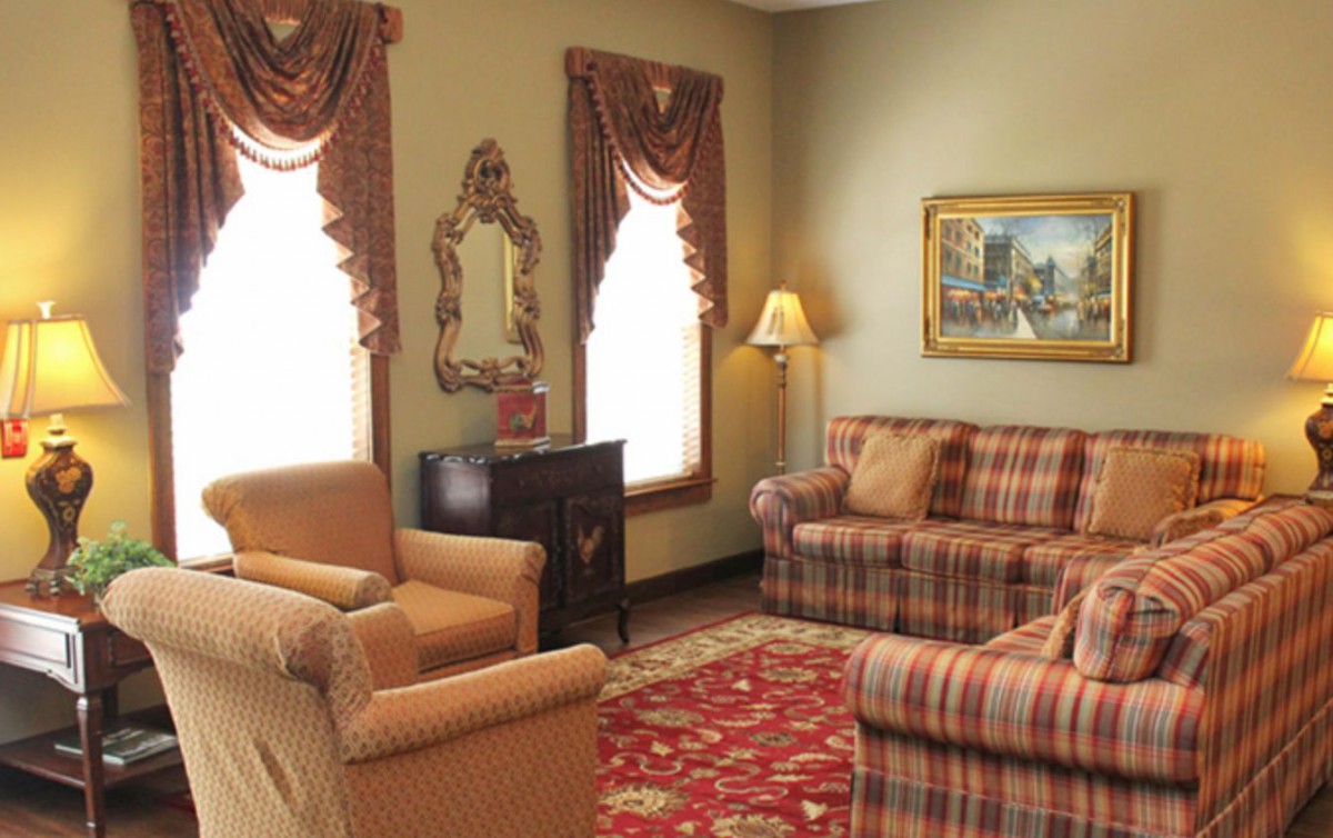 A cozy living room with traditional decor, featuring patterned sofas, armchairs, and a decorative rug.