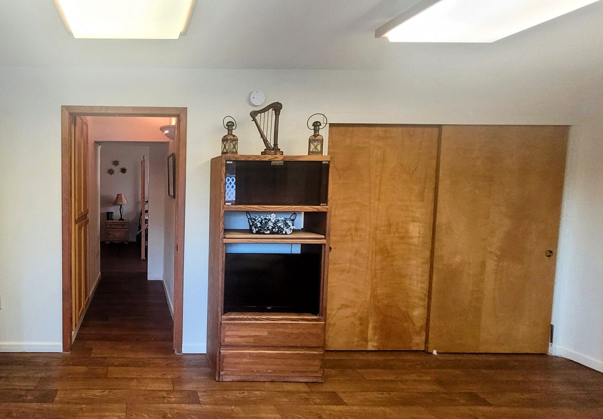 A room with wooden flooring, featuring a cabinet with shelves and closed compartments.