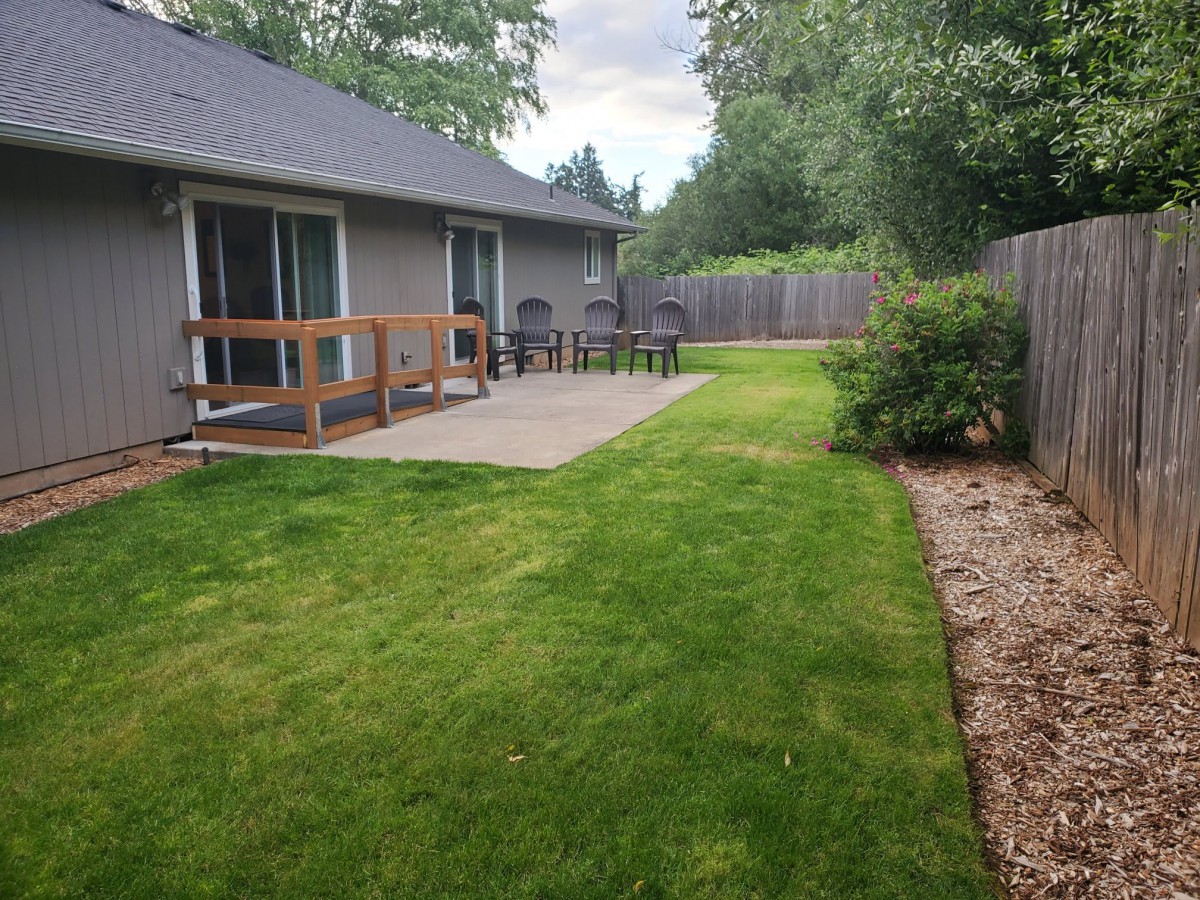 A well-maintained backyard with a grassy lawn, wooden deck, and fences on both sides.