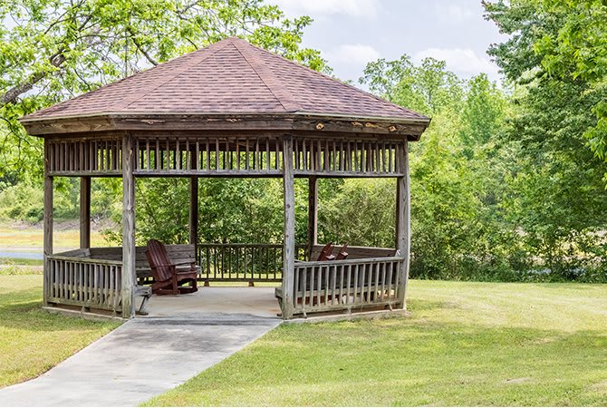 A wooden gazebo in a scenic park setting surrounded by greenery.