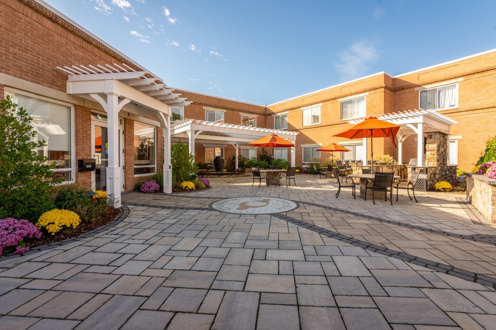 A sunny courtyard with outdoor seating and umbrellas, surrounded by a brick building.