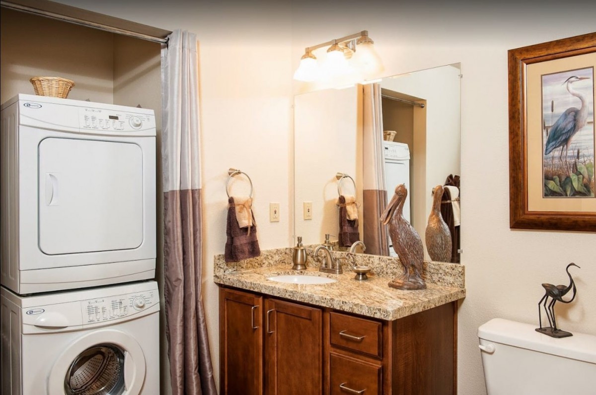 A bathroom with a stacked washer and dryer, a sink with a granite countertop, and a mirror above the cabinet.