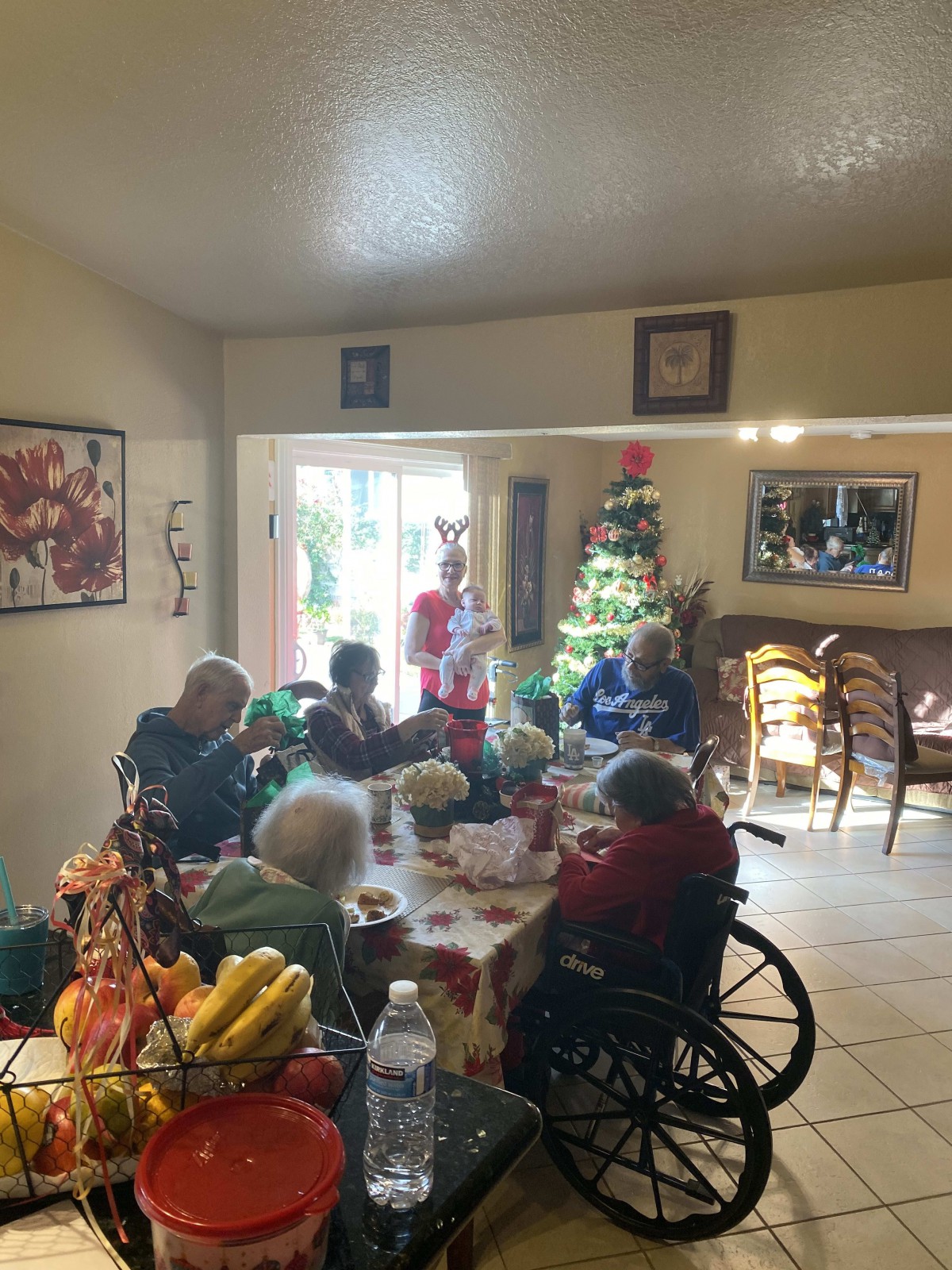 A group of elderly people gathered around a dining table with holiday decorations and a Christmas tree in the background.