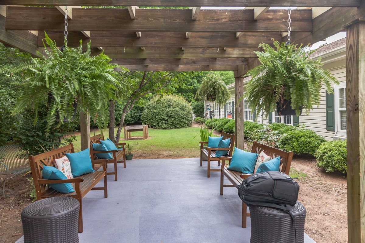 A cozy outdoor patio with a pergola and hanging plants, featuring comfortable seating and garden views.