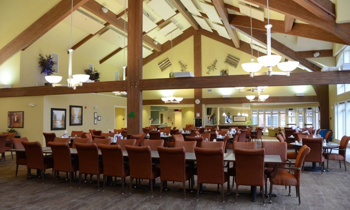 A spacious dining area with long tables and cushioned chairs, featuring high ceilings and elegant chandeliers.