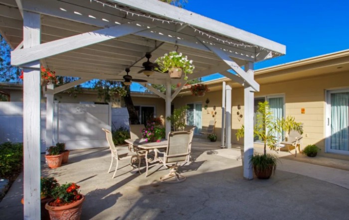A sunny backyard patio with a pergola, outdoor furniture, and hanging plants.