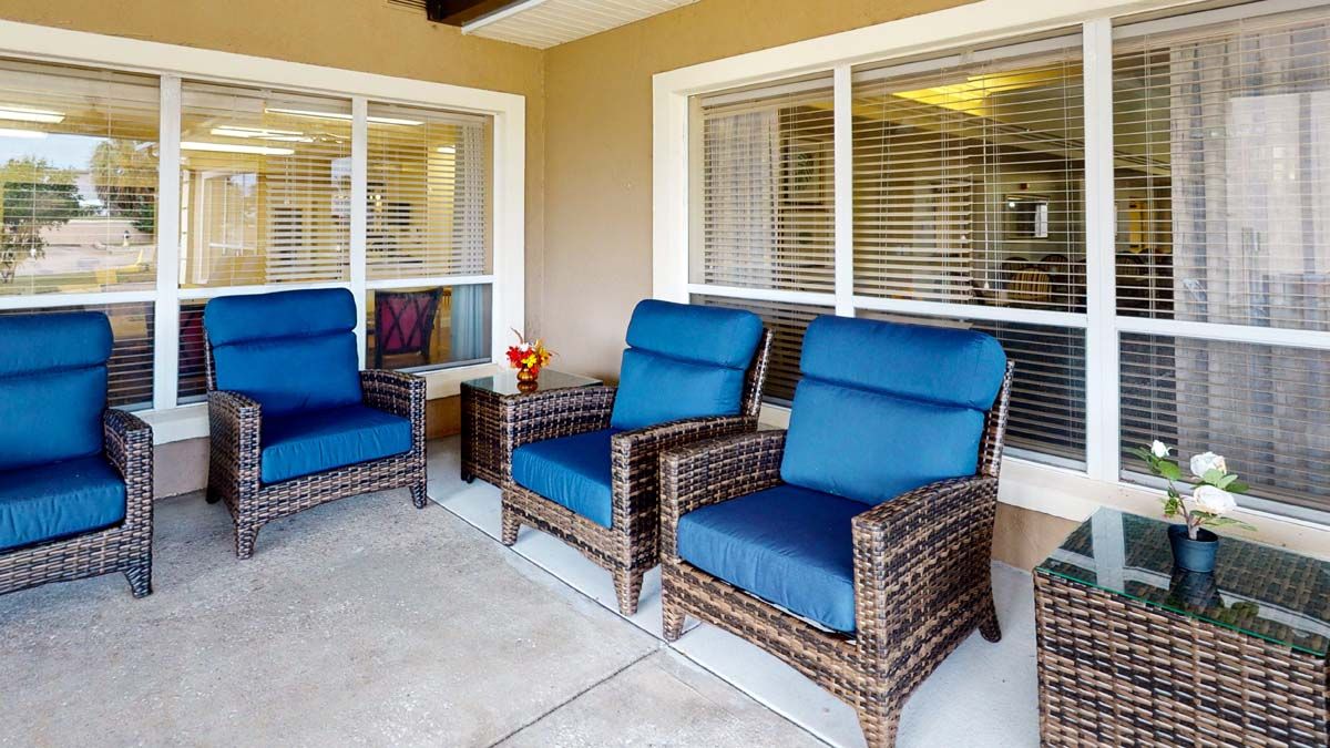 A cozy patio area with wicker chairs featuring blue cushions, set against a windowed wall.