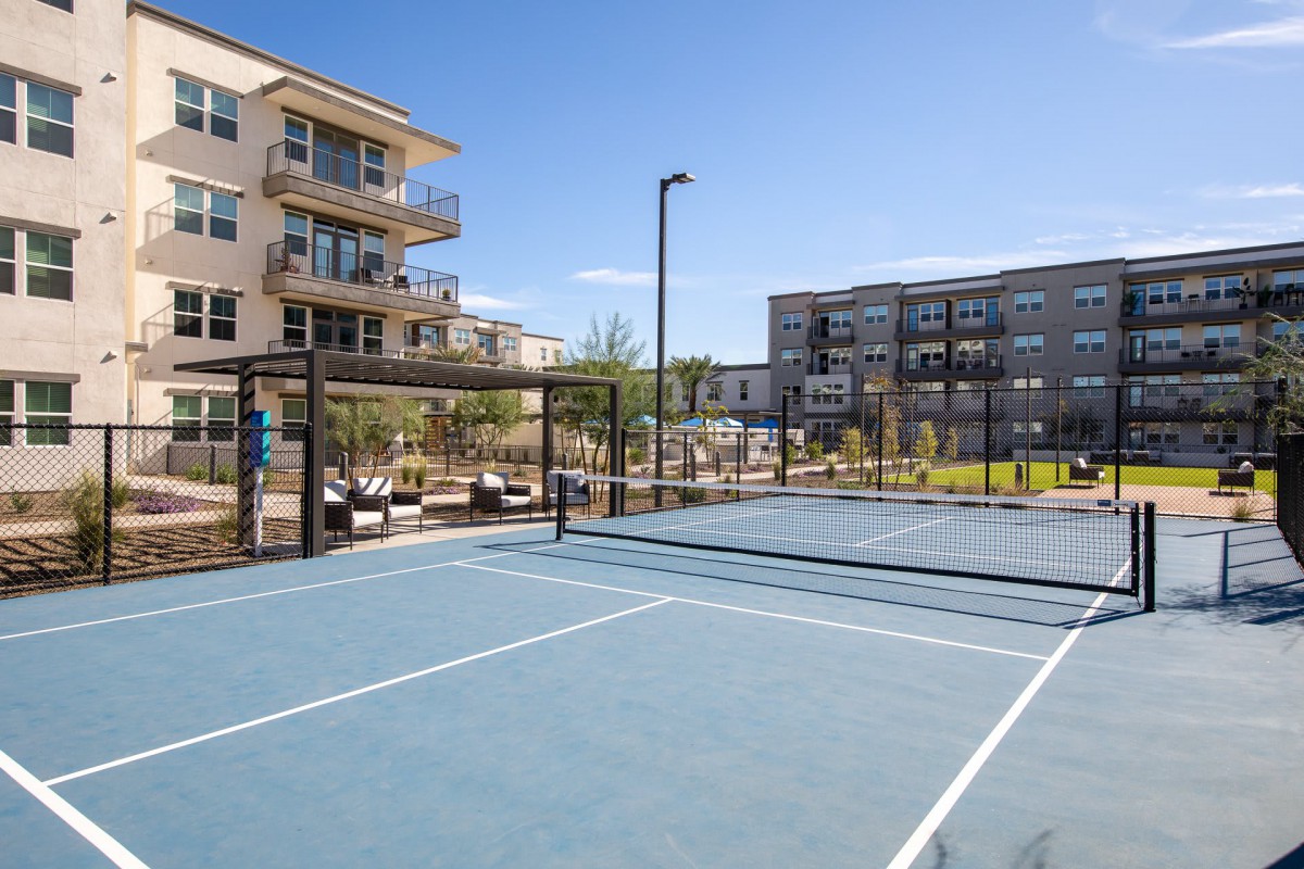 An outdoor tennis court surrounded by modern apartment buildings on a sunny day.