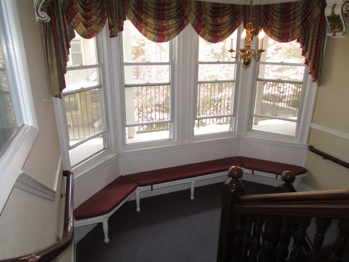 A cozy indoor space with a bay window, featuring built-in red-cushioned seating and decorative curtains overlooking the staircase.
