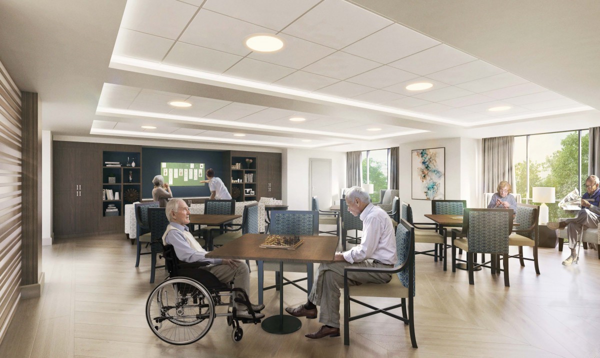 An elderly care home dining area with residents sitting and interacting.
