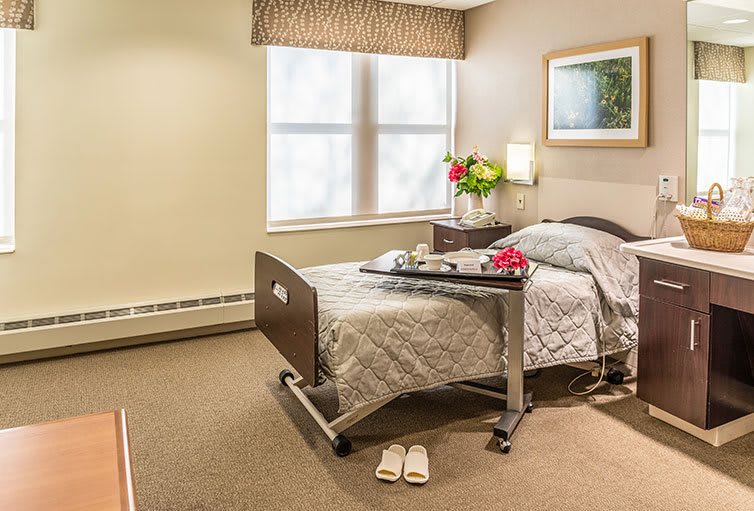A well-lit hospital room with a comfortable bed, tray table, and decorative touches.