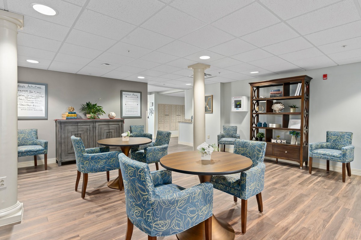 A modern lounge area with tables, chairs, and a bookshelf.