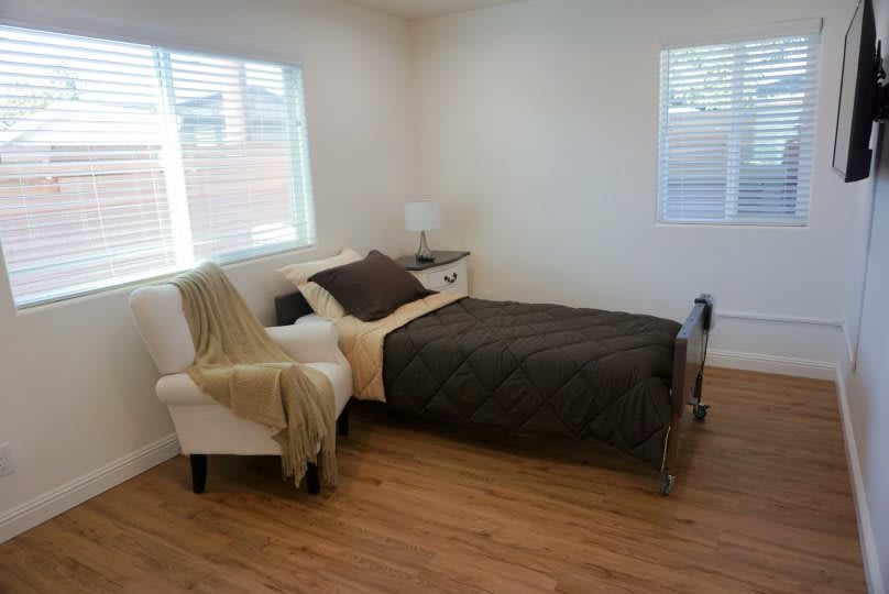 A minimalist bedroom with wooden flooring, featuring a neatly made bed and a cozy chair by the window.