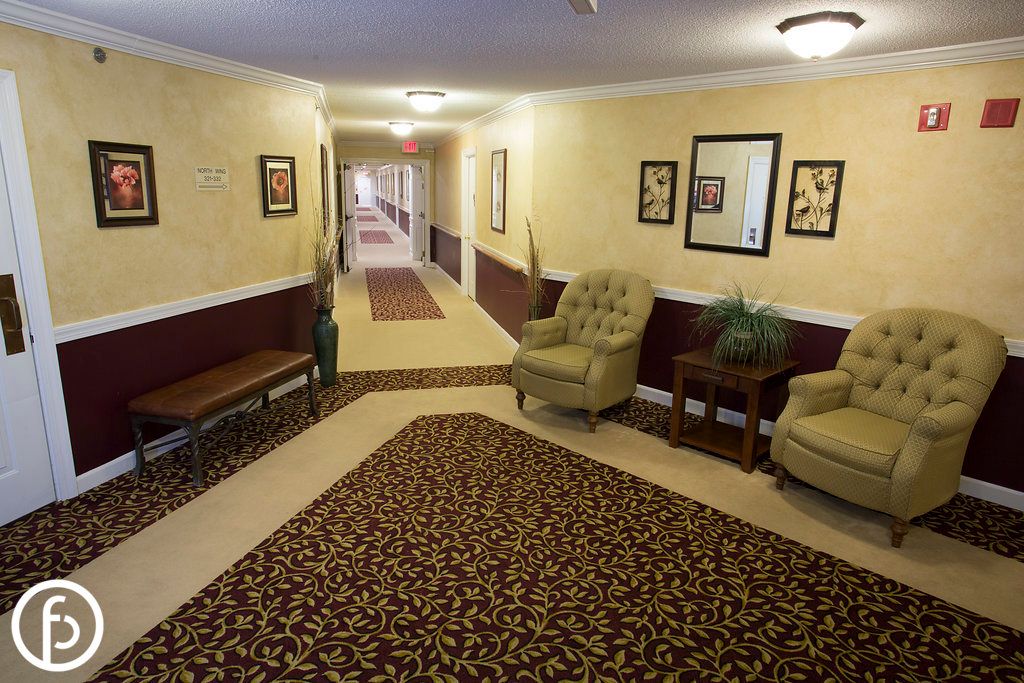 A hotel hallway with a seating area, featuring two armchairs, a side table, and decorative wall art.