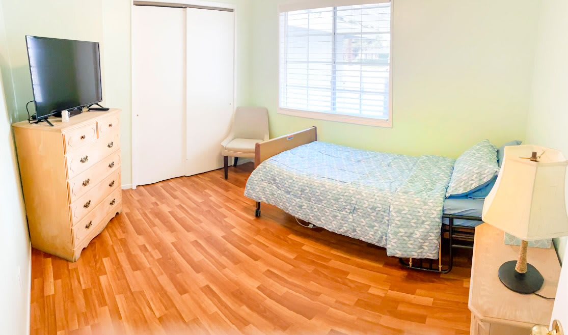A minimalist bedroom with a single bed, chair, and wooden flooring.