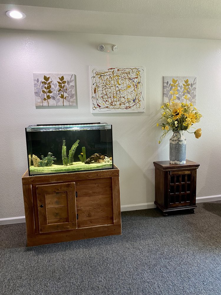 A cozy living room corner featuring a fish tank, vibrant artwork, and a vase of yellow flowers.