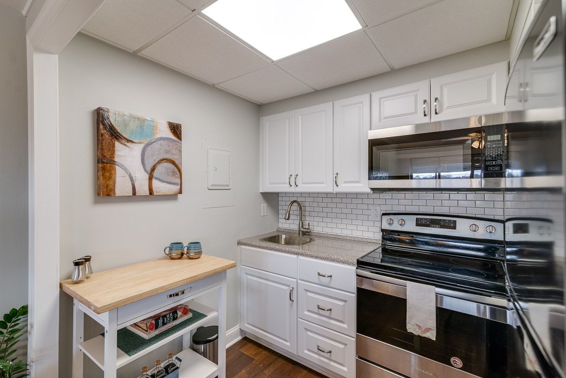A modern kitchen with white cabinets, equipped with a stove, sink, and a small kitchen island.