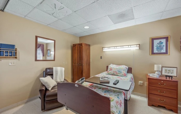 A hospital room featuring a bed, recliner chair, and wooden wardrobe.