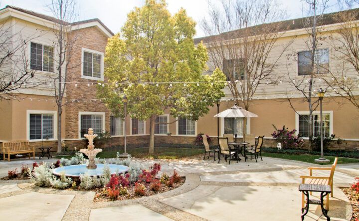 A peaceful courtyard with a fountain, outdoor seating, and lush greenery.
