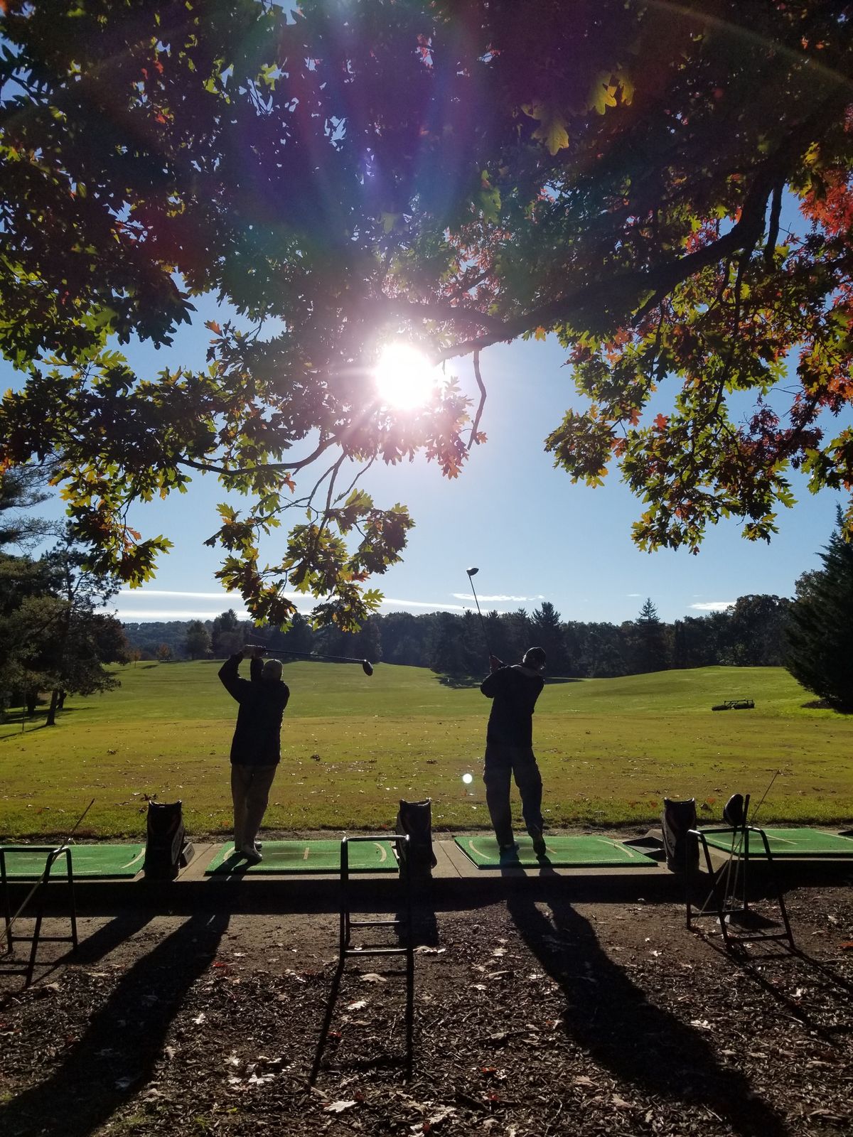 Two people practicing at a driving range under the sunlight.