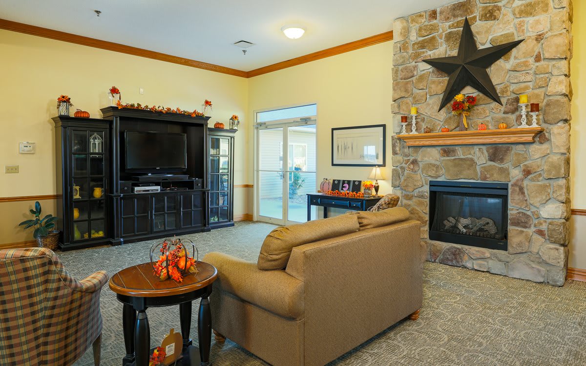 A cozy living room featuring a couch, stone fireplace, television, and decorative elements.