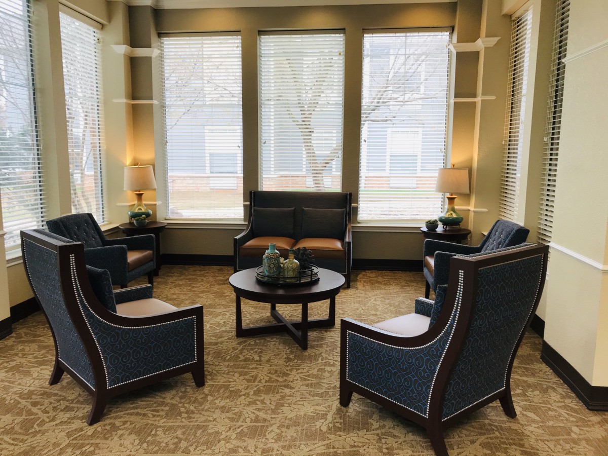 A cozy seating area with armchairs and a coffee table, surrounded by large windows.
