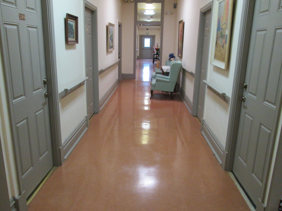 A well-lit hospital hallway with doors on either side and a chair at the end.