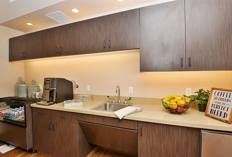 A modern kitchen with wooden cabinets, a coffee maker, a fruit bowl on the counter, and under-cabinet lighting.