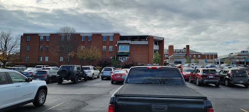 A view of a parking lot filled with various cars, next to a brick building under a cloudy sky.