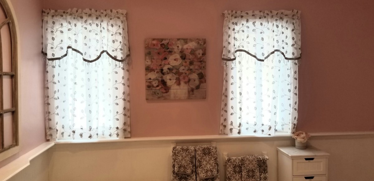 A cozy room featuring two windows with floral curtains and a central floral wall art piece.