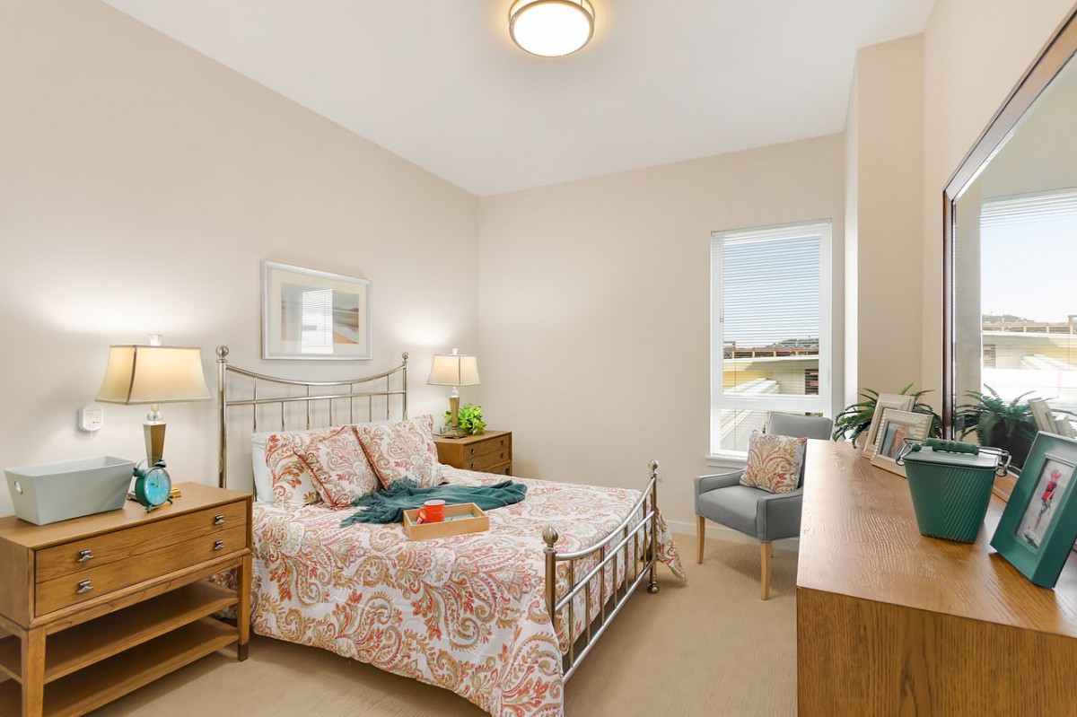 A cozy bedroom with a decorative bedspread, wooden furniture, and a window allowing natural light.