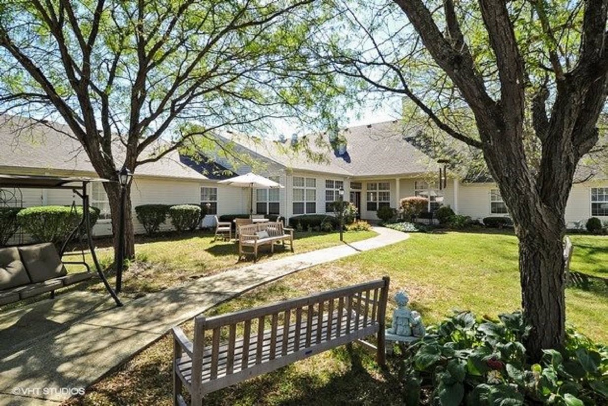 A peaceful backyard with a wooden bench and patio area surrounded by trees.