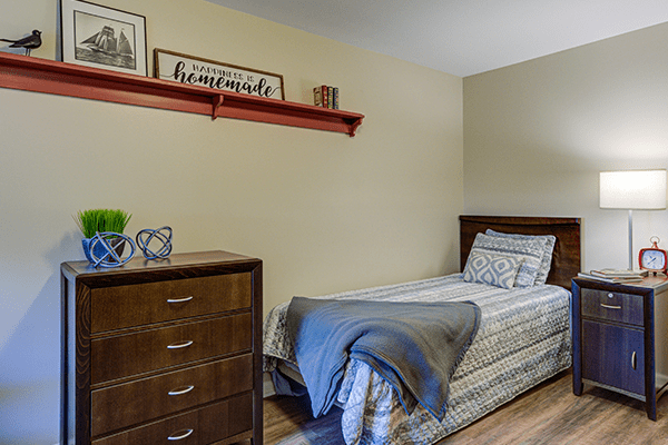A cozy bedroom with a single bed, dresser, and decorative shelf.