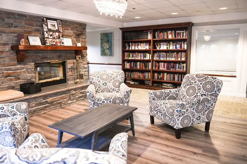 A cozy reading room featuring armchairs, a fireplace, and a bookshelf filled with books.