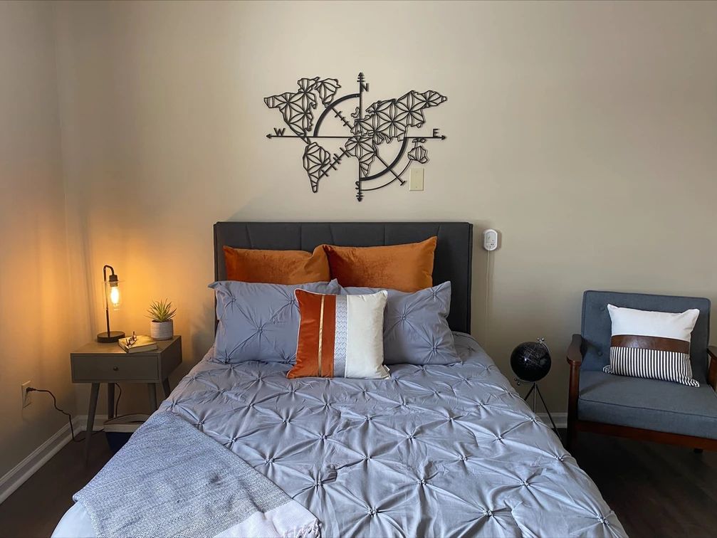 A cozy bedroom with a well-made bed, featuring contrasting pillows and unique wall art.