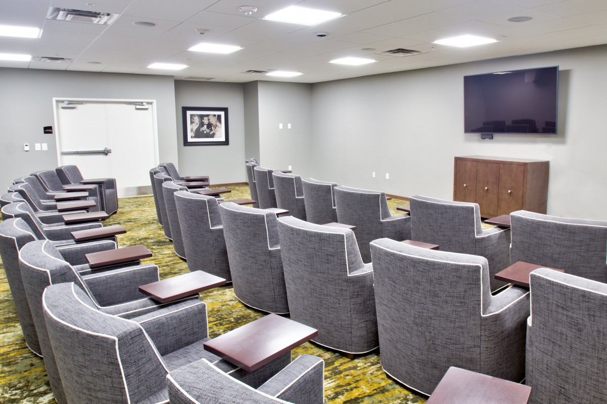 A small theater or conference room with multiple rows of gray chairs facing a screen.