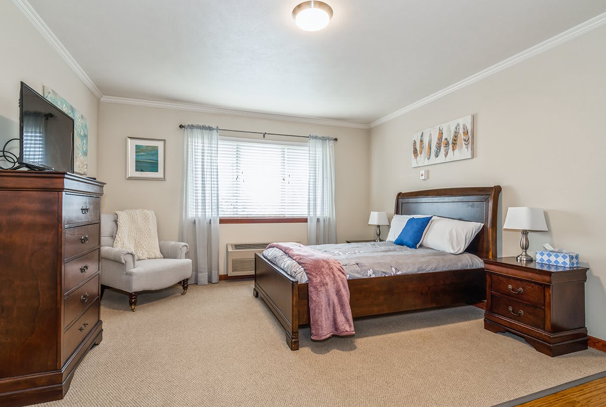 A cozy bedroom featuring a bed with wooden frame, armchair, and decor accents.