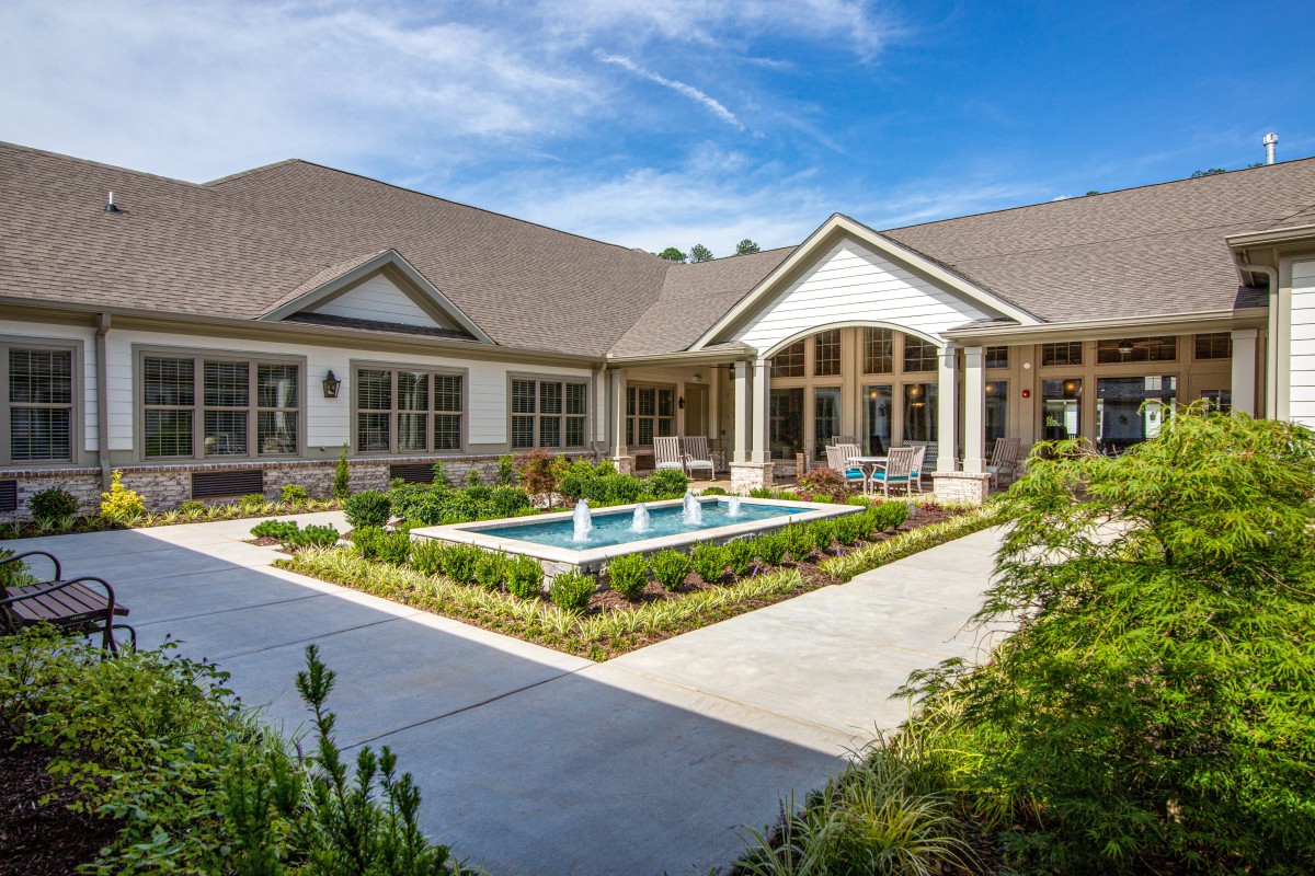 A beautiful house with a landscaped garden and a small central pool under a clear blue sky.