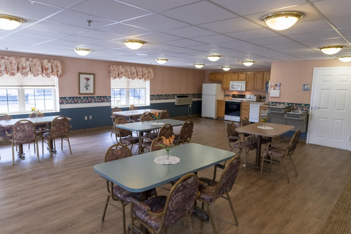 A spacious dining room with several tables and chairs, adjacent to a kitchen area.