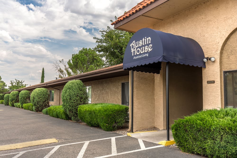 A hotel entrance featuring a blue awning and well-maintained landscaping.