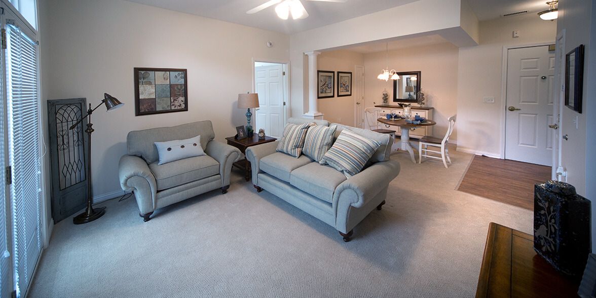 A cozy living room with a sofa and armchair, leading into a dining area.