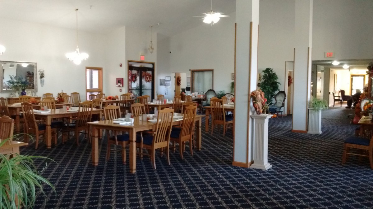 An indoor dining area with wooden tables and chairs arranged on a carpeted floor.
