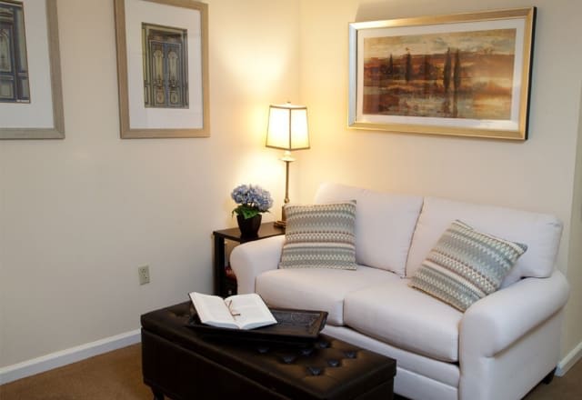 A cozy living room with a white sofa, accented by striped cushions, a table lamp, and framed artwork on the walls.