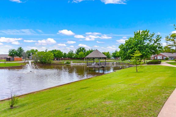 A peaceful park scene with a gazebo by the lake under a bright blue sky.